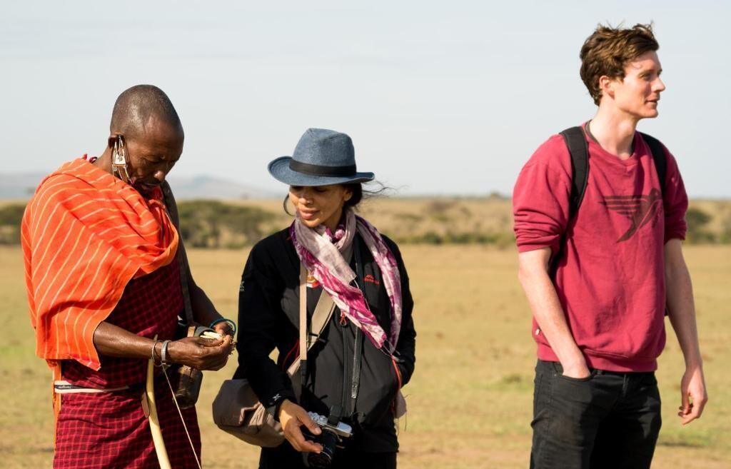 Three people in an outdoor setting, one in traditional attire, another in casual clothing, and the third in a red shirt.