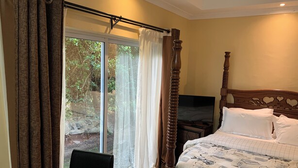 A bedroom with a bed, a TV, and a sliding glass door leading to a balcony. - Nairobi Inn (Syokimau)