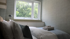 Una camera da letto con un letto, cuscini, una finestra e un termosifone.