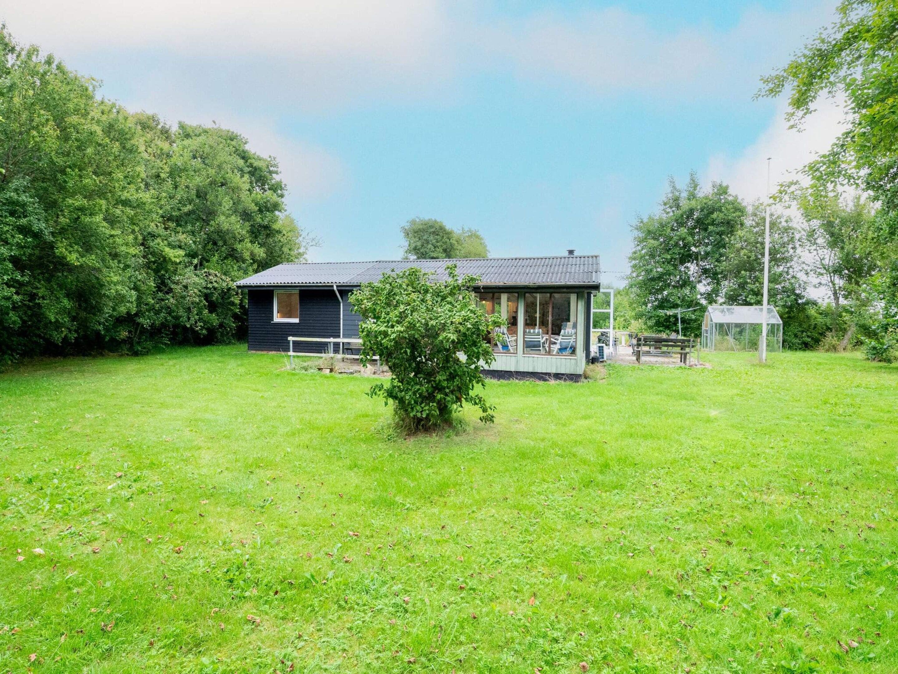 A small house with a porch, surrounded by a grassy yard and trees.