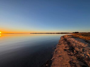 Un lac paisible au coucher du soleil, avec une rive sablonneuse.