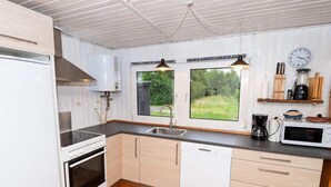 Eine moderne Küche mit weißen Schränken, Backofen, Geschirrspüler, Spüle und einem Fenster mit Blick auf Grünflächen.