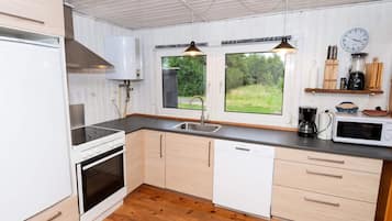 Cozinha moderna com armários brancos, forno embutido, lava-louças, pia e janela com vista para o verde lá fora.