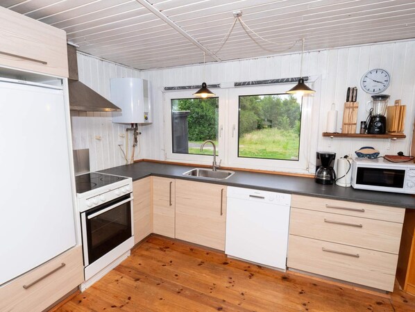 A modern kitchen with white cabinetry, a built-in oven, a dishwasher, a sink, and a window providing a view of greenery outside. - 6 Person Holiday Home in Thyholm (Thyholm)