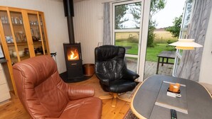 Ein gemütliches Wohnzimmer mit Kamin, Ledersesseln, einem runden Tisch und Blick ins Freie.
