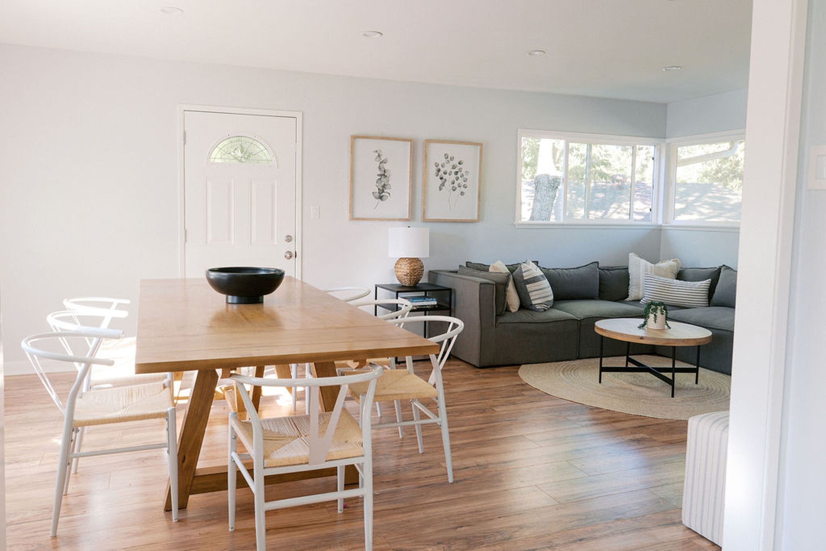 Ein stilvolles Wohnzimmer mit einem Holzesstisch, weißen Stühlen, einem grauen Sofa und einem kleinen runden Couchtisch.