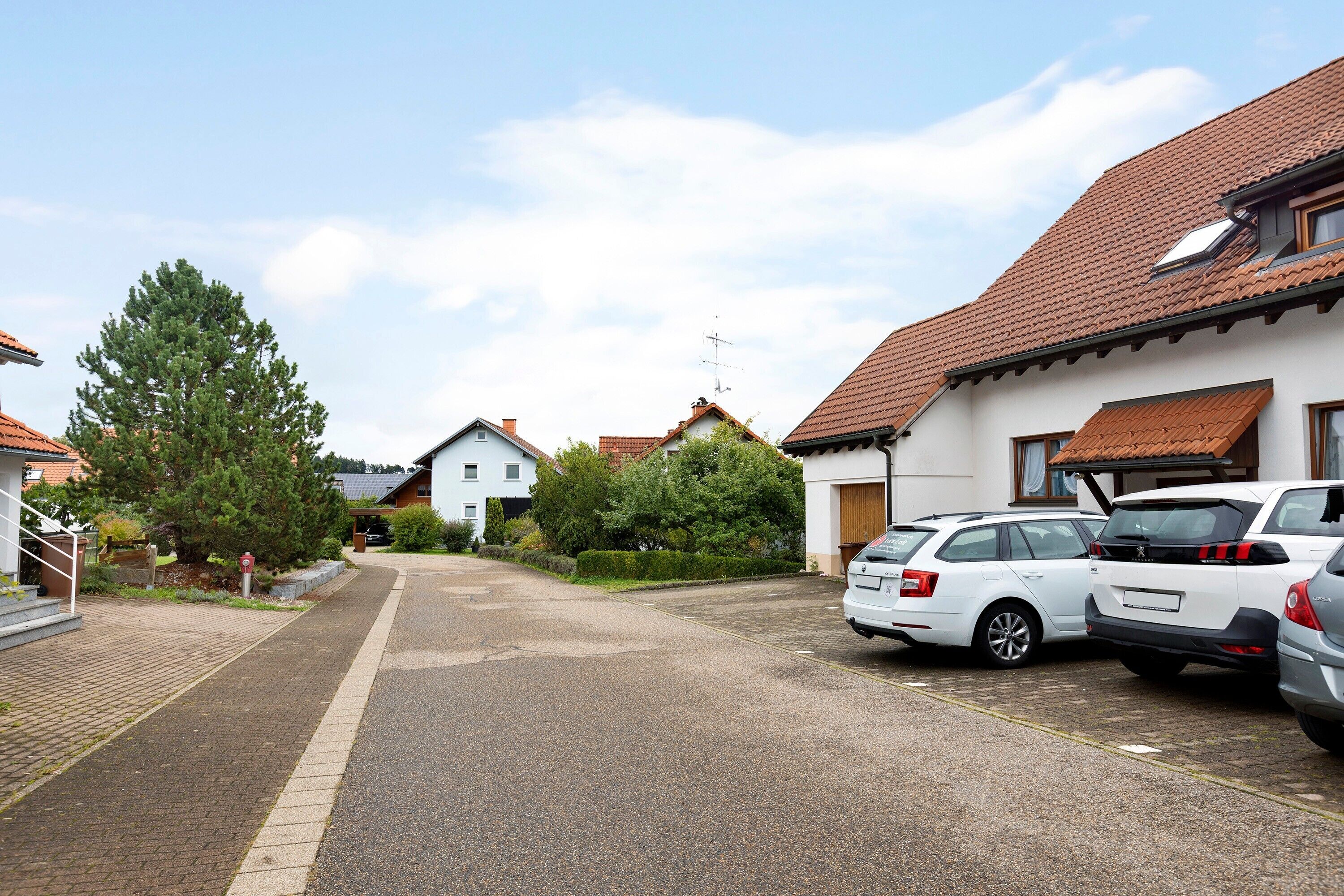 Eine Wohnstraße mit parkenden Autos, Häusern mit roten Ziegeldächern und blauem Himmel.