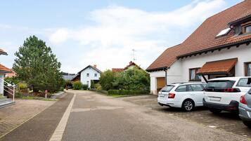 Eine Wohnstraße mit parkenden Autos, Häusern mit roten Ziegeldächern und blauem Himmel.