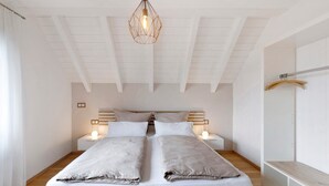 En dubbelsäng med två sängbord, en hängande lampa och en träbänk.