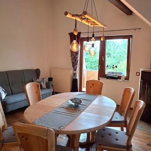 A dining area with a round wooden table, cushioned chairs, a hanging light fixture, and a view of greenery through a window. - Maisonette 'Lufs Loft' with Garden View, Balcony, Up to 6 Guests (Ühlingen-Birkendorf)