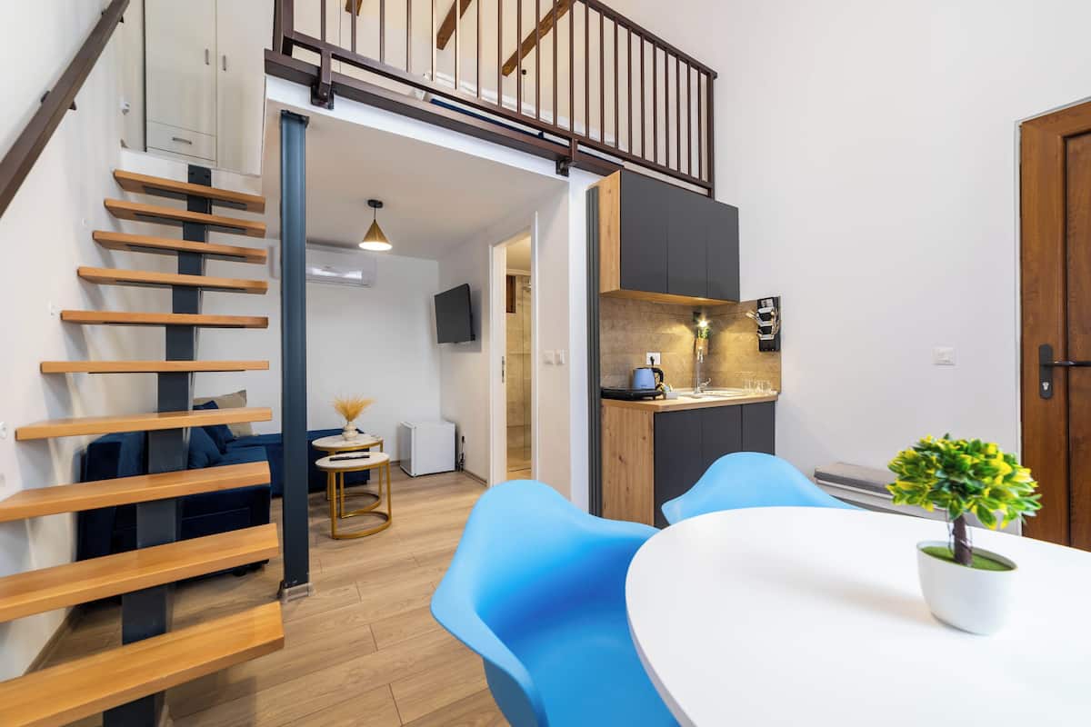 A modern kitchen with a built-in stove, a dining area with blue chairs, a wooden staircase, and a small potted plant on the table.