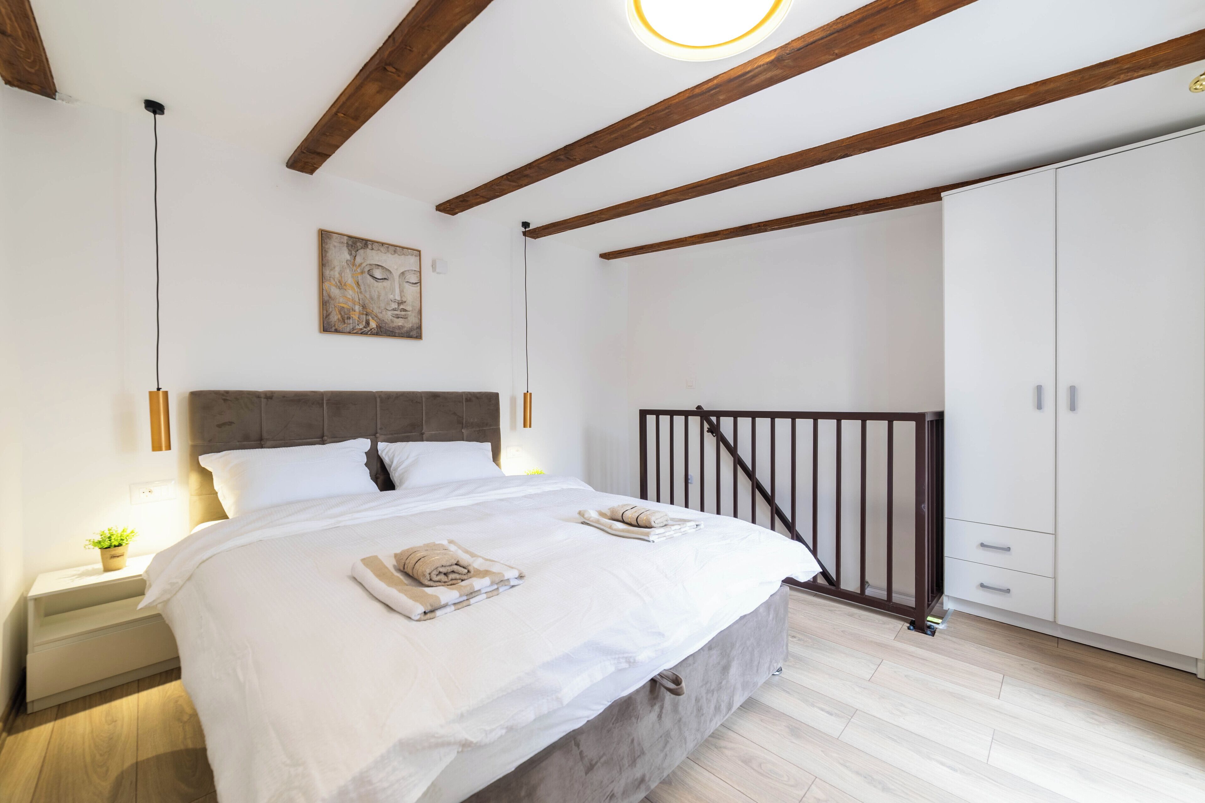 Un dormitorio con cama, mesitas de noche, armario y una obra de arte en la pared, además de una barandilla de escalera.