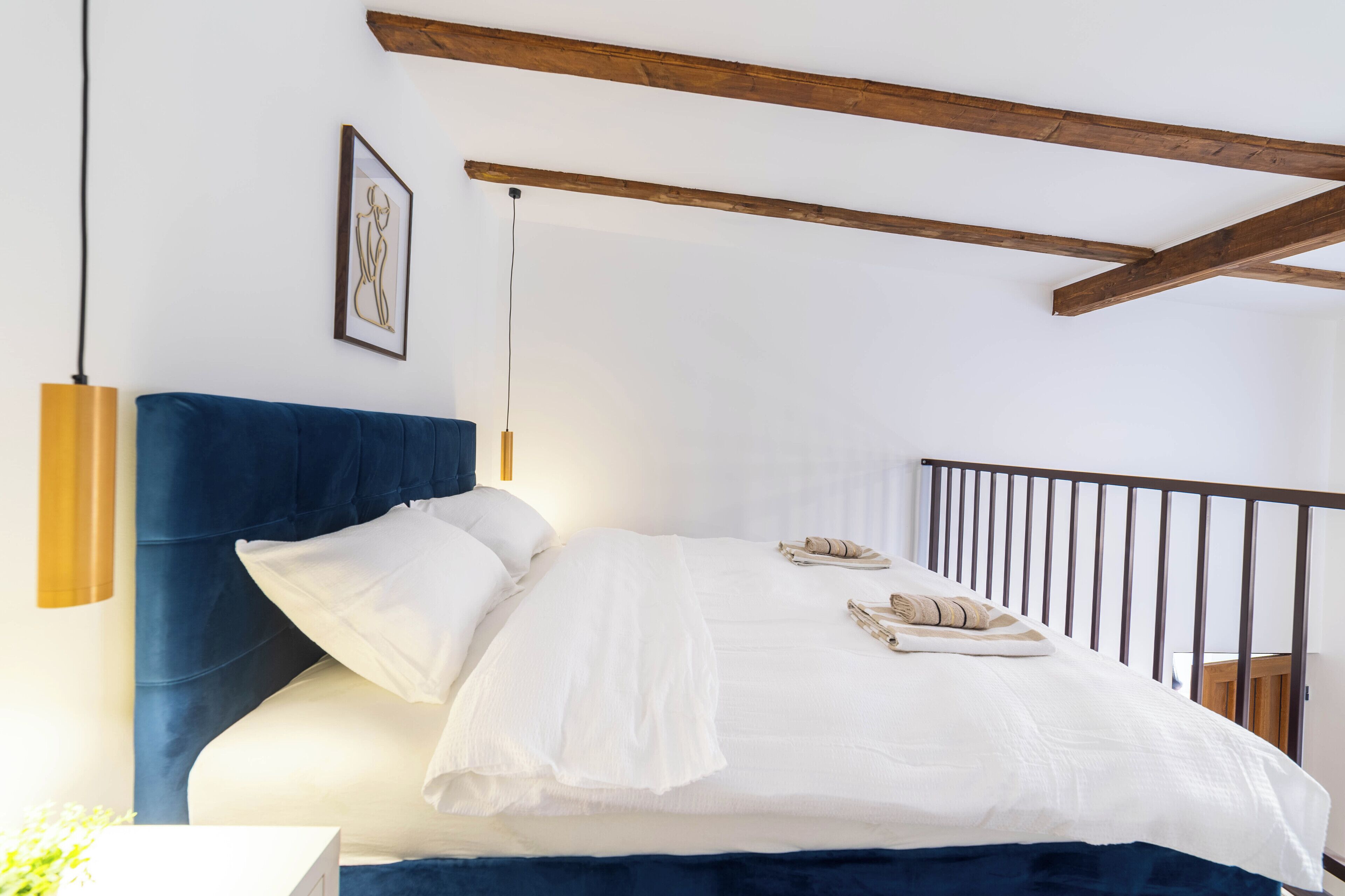Une chambre à coucher avec un lit, une lampe de chevet, un tableau encadré au mur et une poutre en bois au plafond.