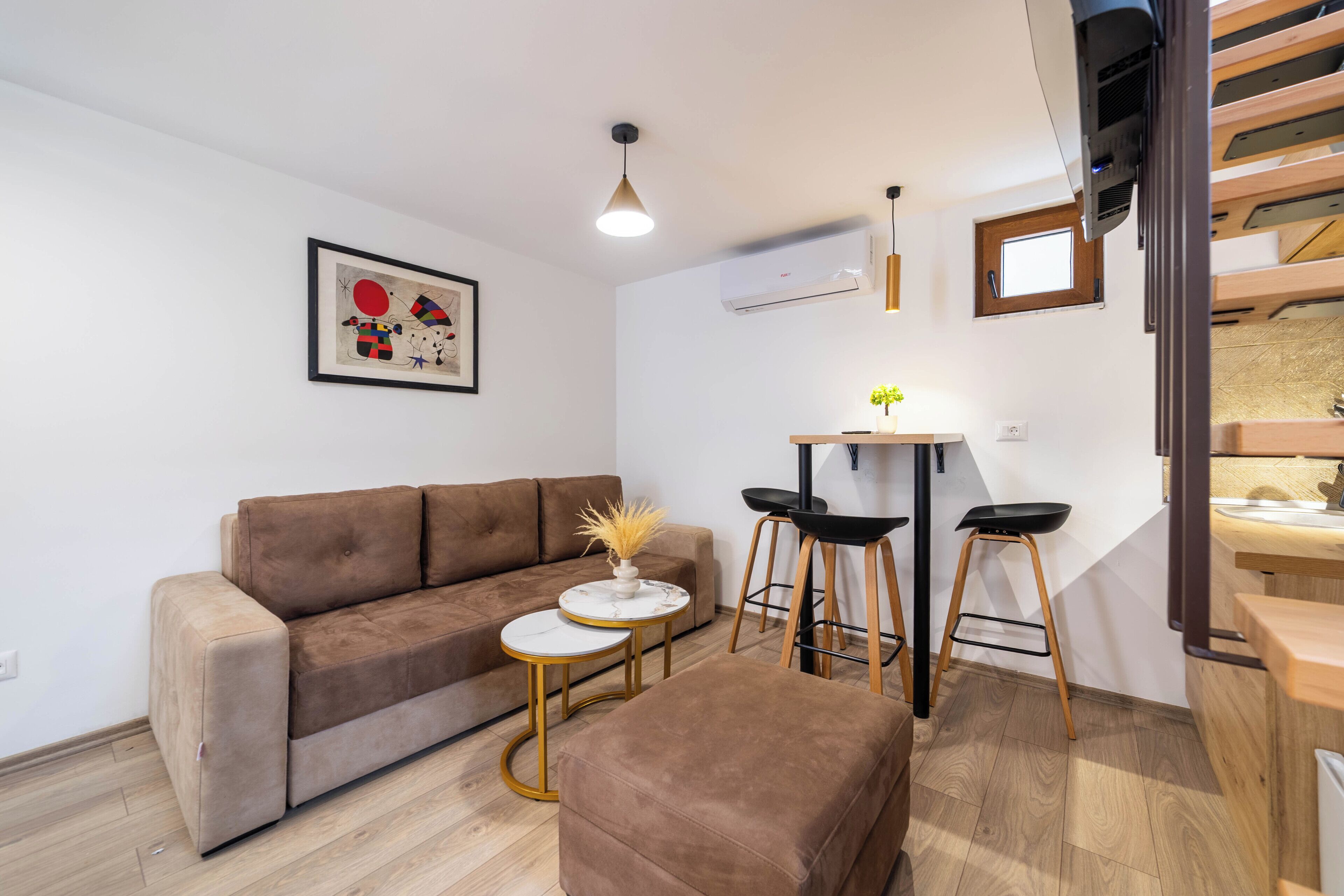 A modern living room with a brown sofa, a small round table with a vase, and two black bar stools.