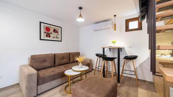 A modern living room with a brown sofa, a small round table with a vase, and two black bar stools.