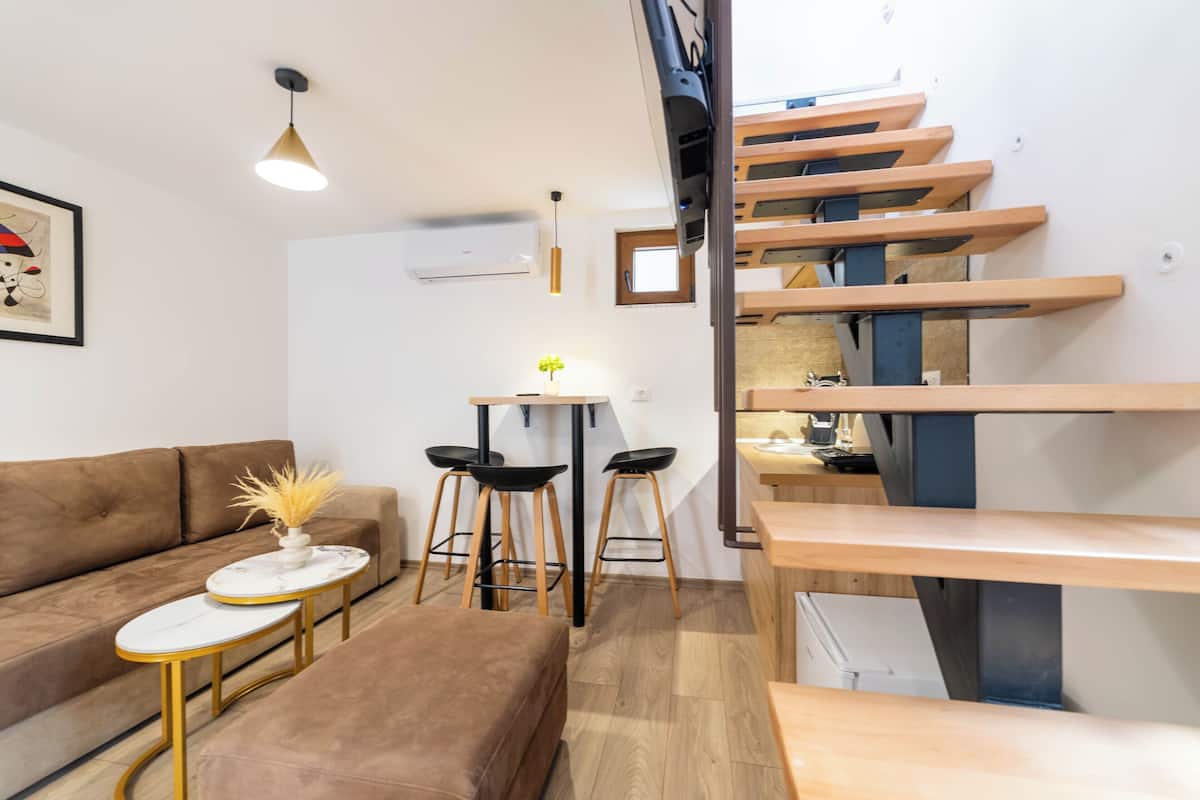 A modern living room with a brown sofa, a small round table with a vase, and a staircase with wooden steps.