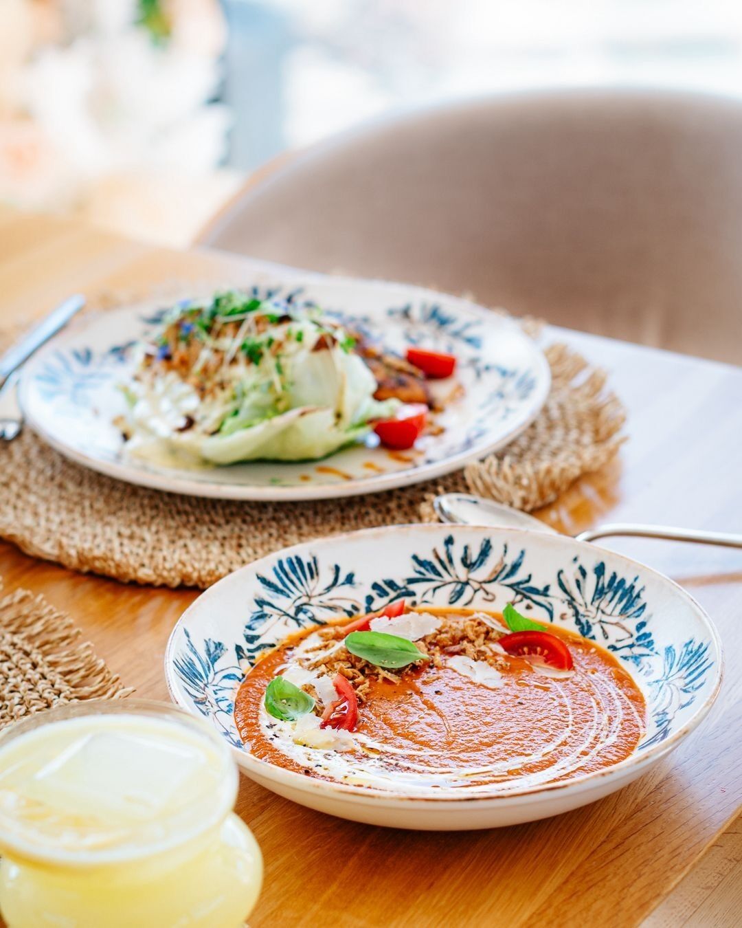 Two plates of food on a wooden table with a woven placemat.