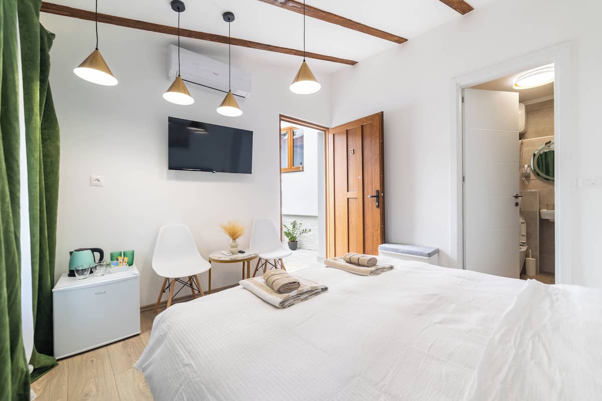 A modern hotel room with a bed, a desk, a TV, and a shower area.