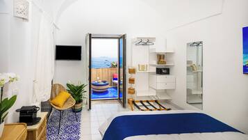 A modern bedroom with a bed, a TV, a wardrobe, and a view of the sea through an open door.