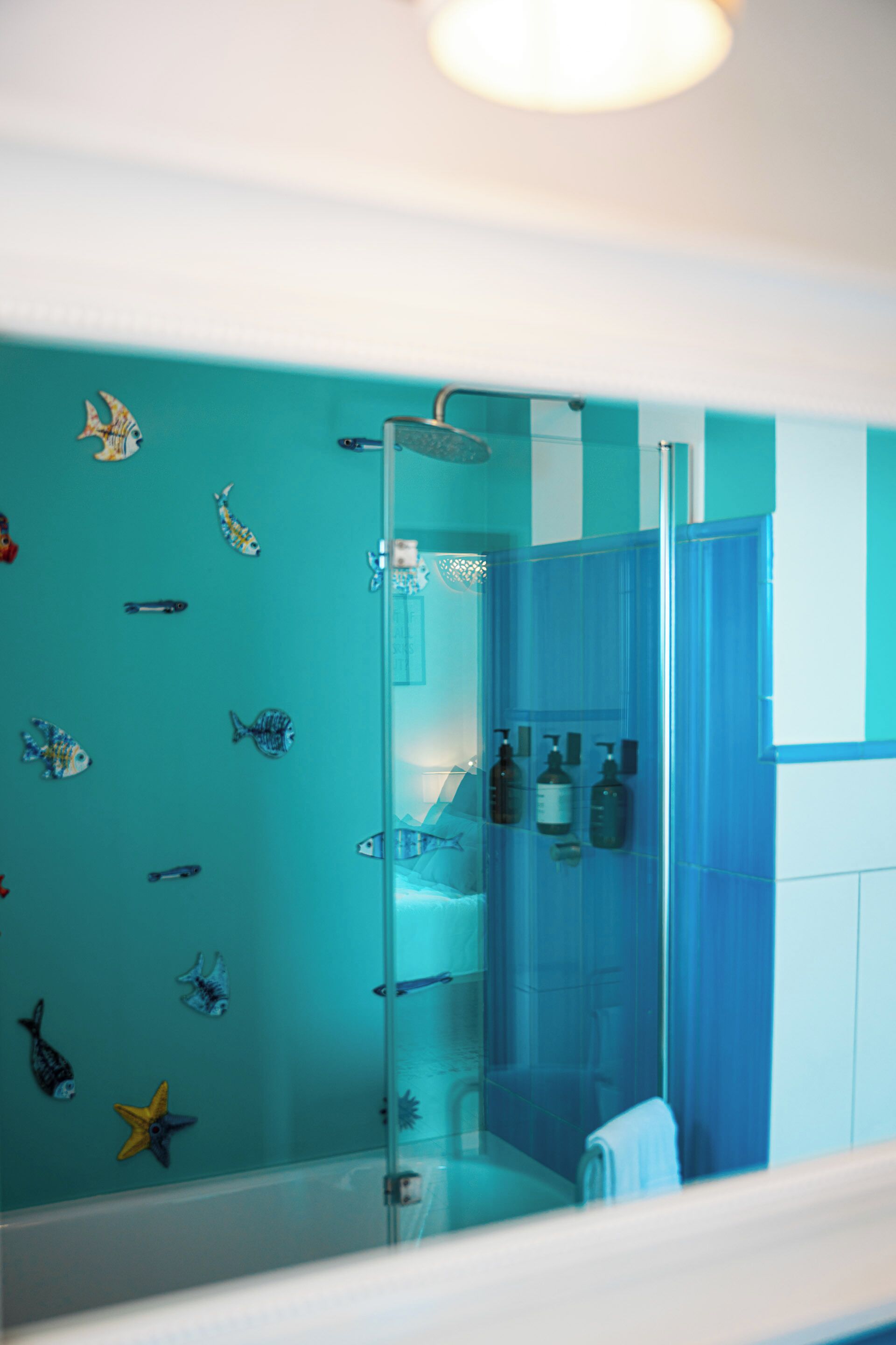 A bathroom with a glass shower enclosure, a sink with toiletries, and a wall decorated with fish decals.