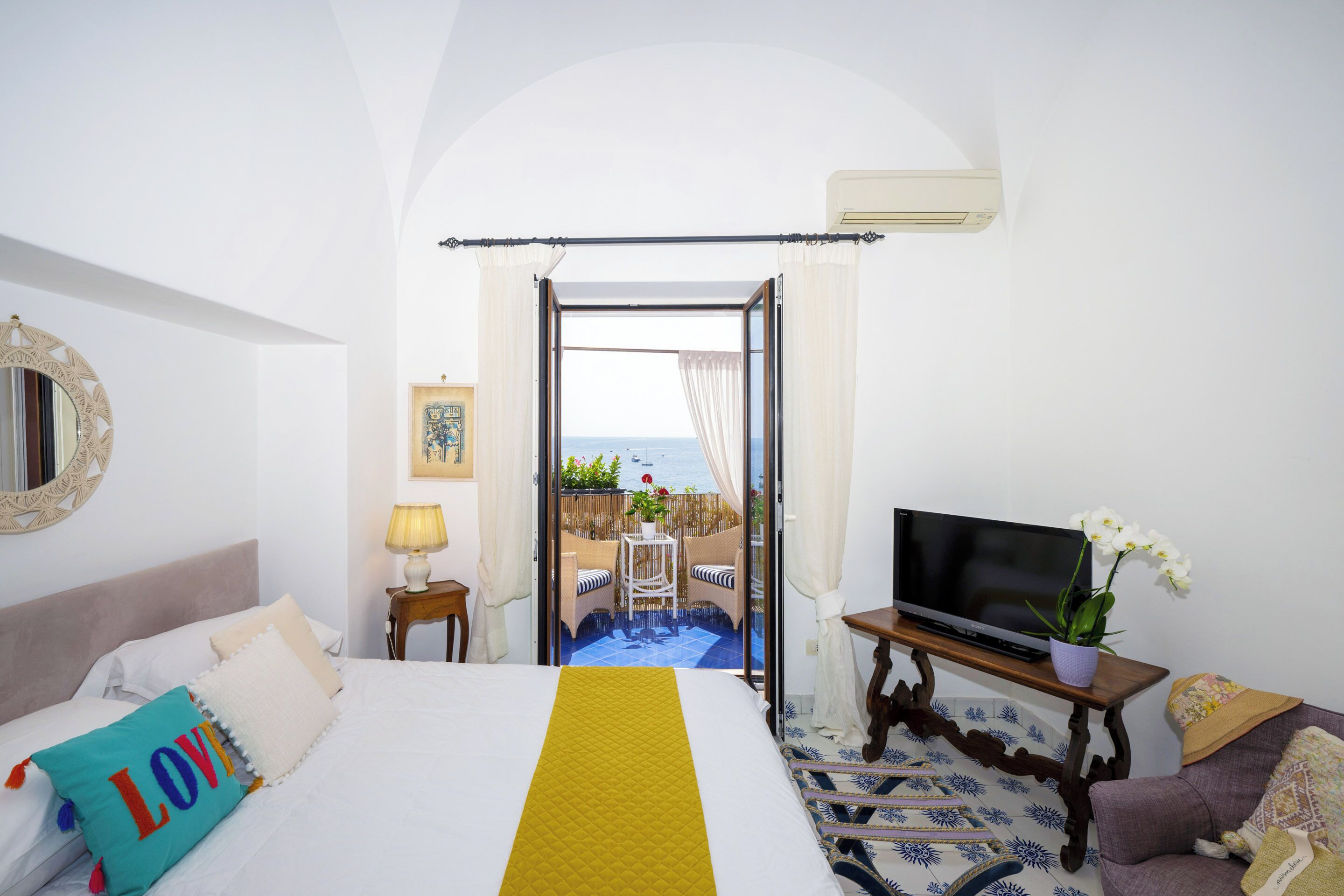 A hotel room with a bed, TV, and a balcony with a view.