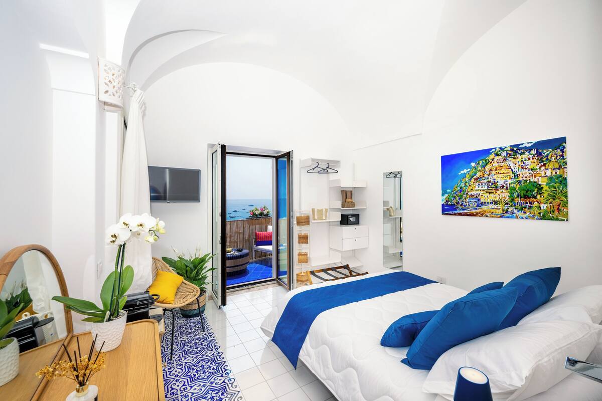 A modern bedroom with a bed, a TV, a balcony with a view, and a painting on the wall.