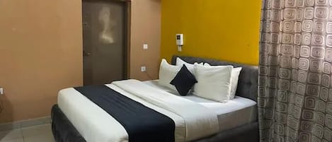 A bedroom with a bed, an air conditioning unit, a door, and a patterned curtain.