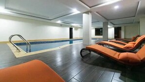 A swimming pool area with a diving board, lounge chairs, and a tiled floor.