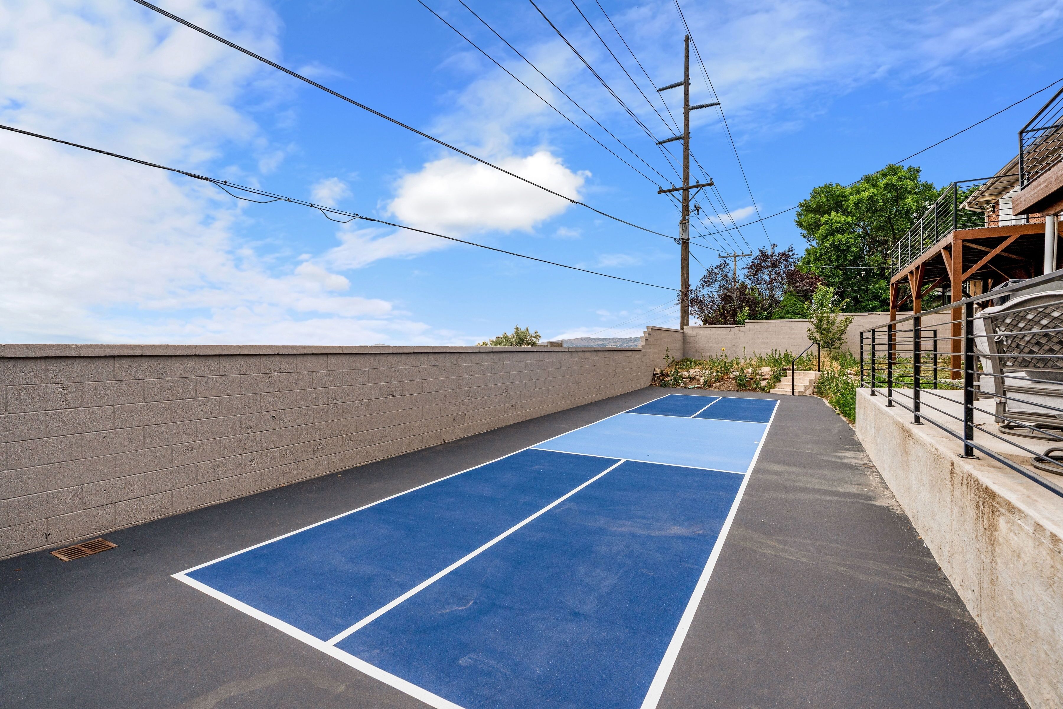 A tennis court with a blue surface and white boundary lines, adjacent to a brick wall and a metal fence.