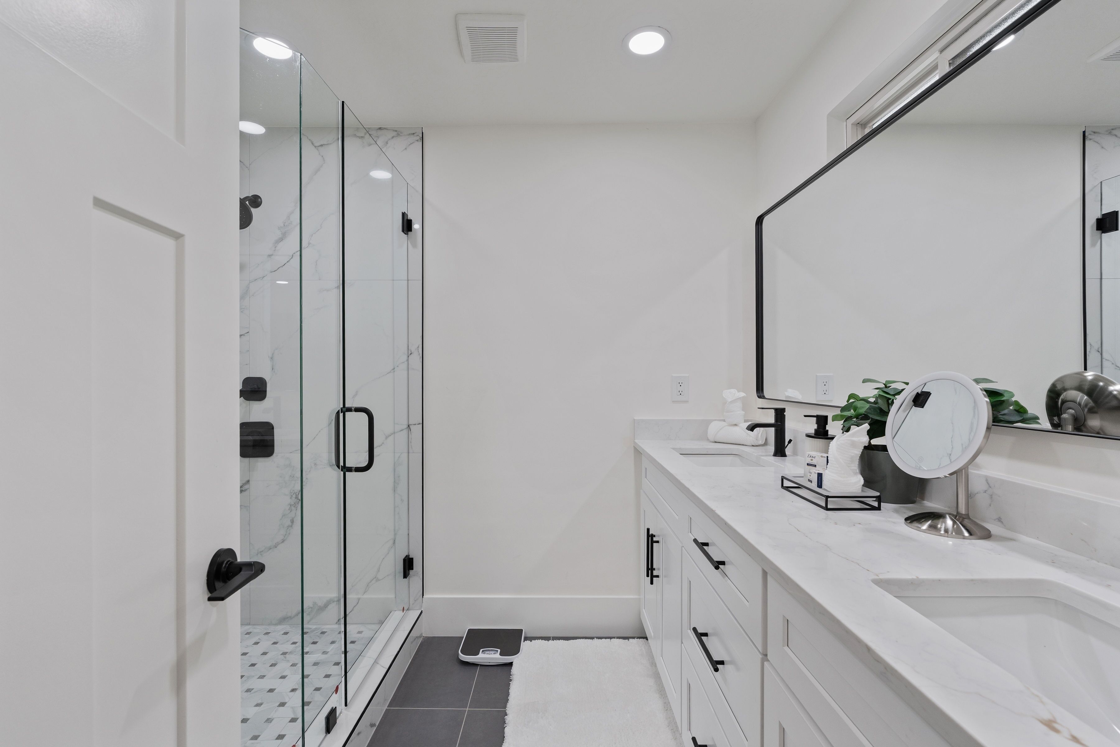 A modern bathroom with a glass shower enclosure, a white marble sink, and a large mirror.