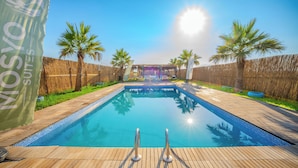 Una piscina con cubierta de madera, palmeras y una cerca.