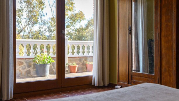 A room with a wooden door, a window with a view of a balcony, and a potted plant on the balcony. - Caballo Tourist Apartment (Lanjarón)