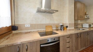 A kitchen with a built-in stove, a microwave, wooden cabinets, and a stainless steel range hood. - Caballo Tourist Apartment (Lanjarón)
