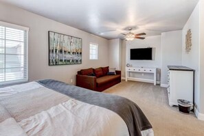 Een slaapkamer met een groot bed, een rode bank, een plafondventilator, een aan de muur bevestigde televisie en een klein kastje.