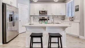 A modern kitchen with white cabinets, stainless steel appliances, and two bar stools.