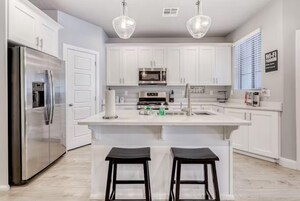 A modern kitchen with white cabinets, stainless steel appliances, and two bar stools.