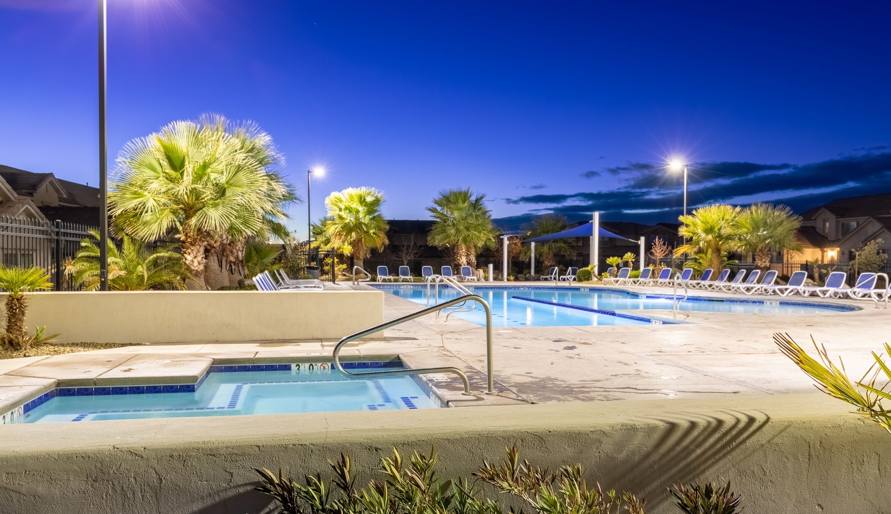 A swimming pool area with multiple lanes, lounge chairs, and palm trees.