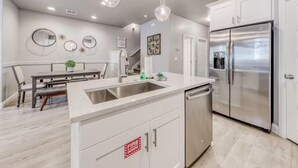 A modern kitchen with white cabinets, a stainless steel refrigerator, a sink, and pendant lights.