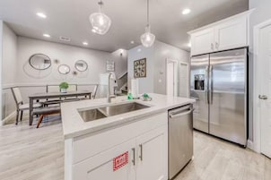 A modern kitchen with white cabinets, a stainless steel refrigerator, a sink, and pendant lights.
