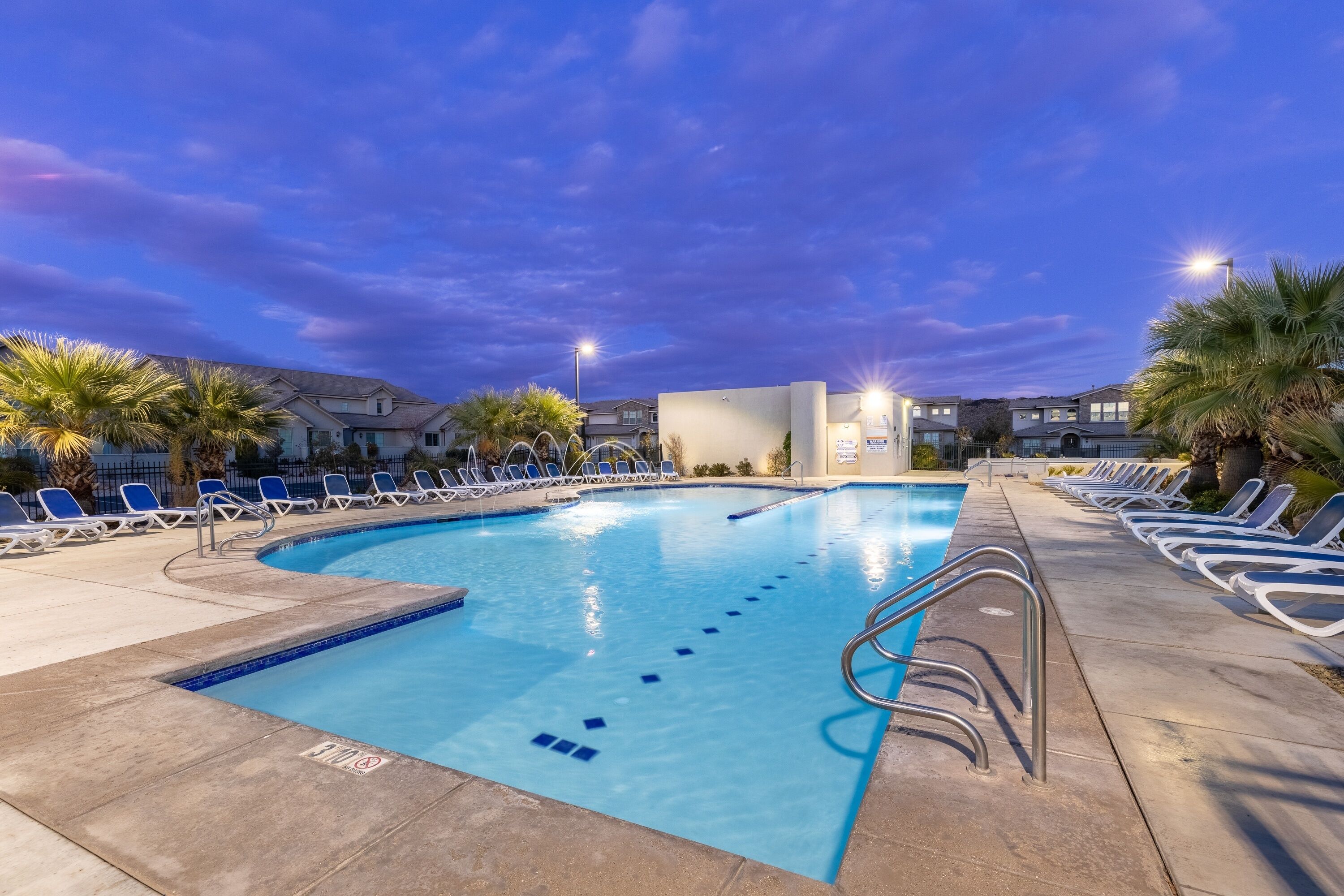 A swimming pool with blue tiles, surrounded by lounge chairs and palm trees.
