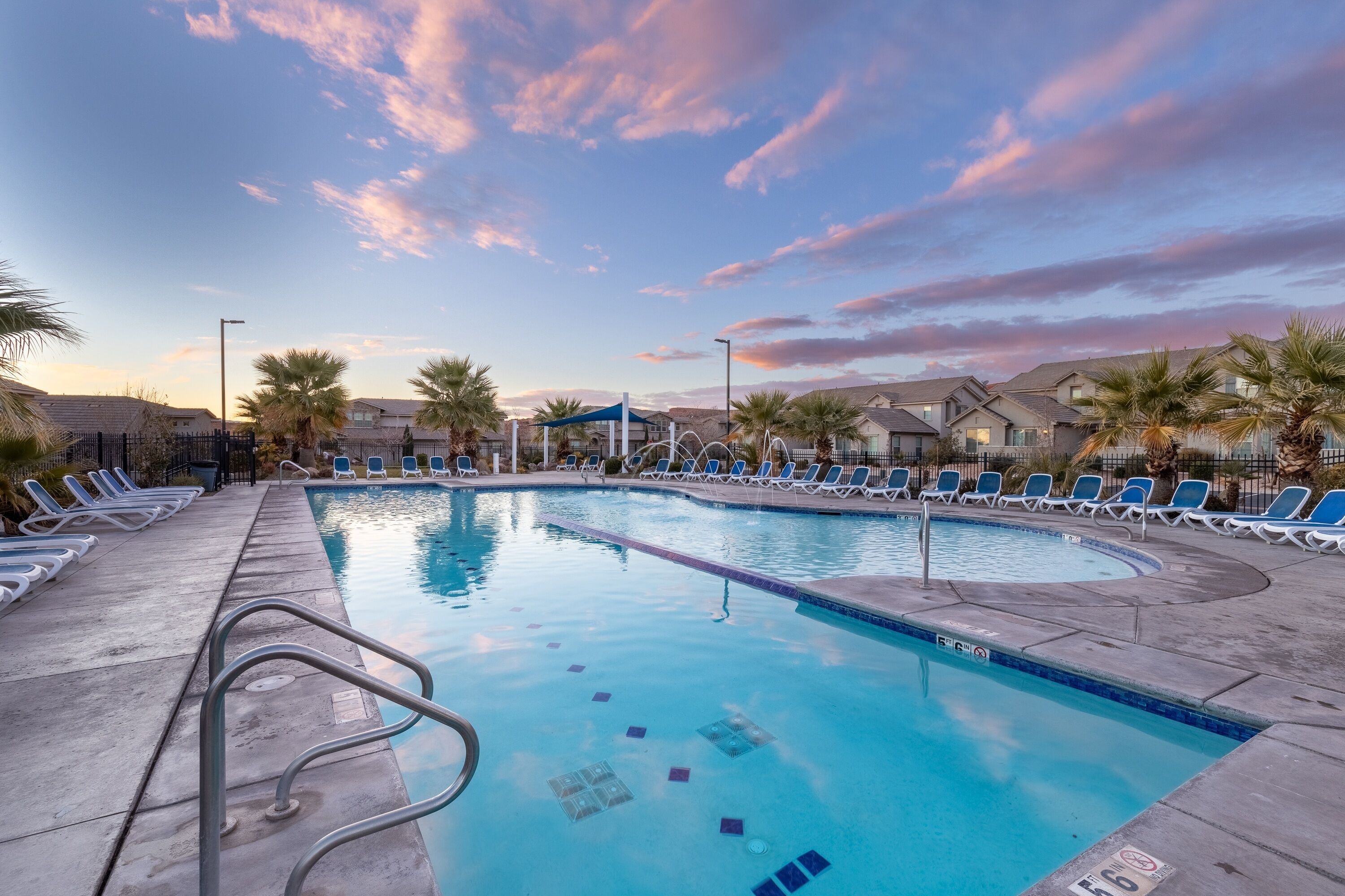 A swimming pool with lounge chairs and palm trees, surrounded by buildings.