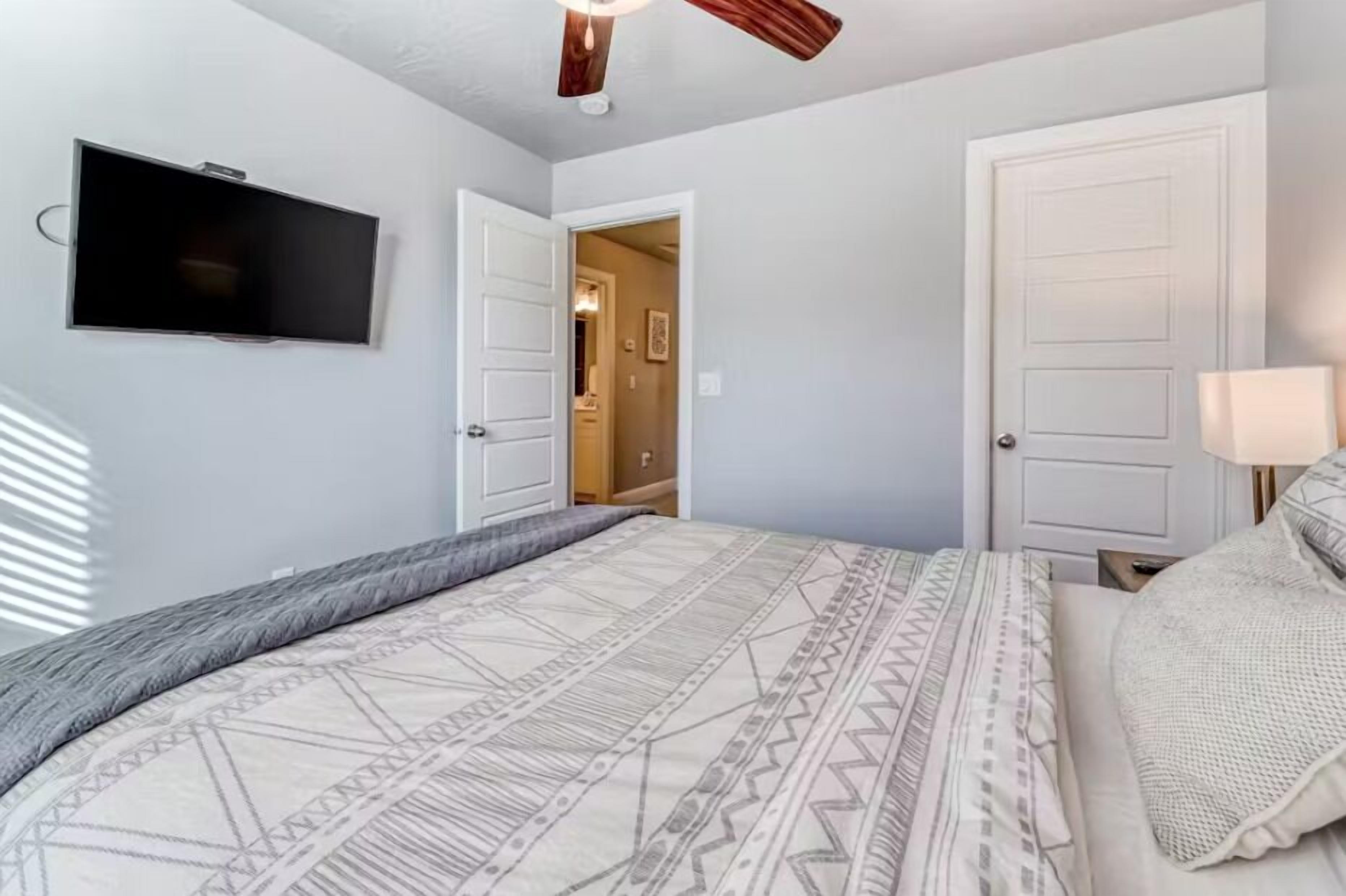 A bedroom with a bed, a TV mounted on the wall, and a door leading to another room.