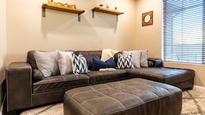 A living room with a sectional sofa, a matching ottoman, and two wall-mounted shelves with plants. - Sand Cove 3 Bedroom Townhouse (Washington)