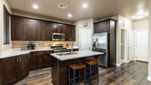 A modern kitchen with dark wood cabinets, stainless steel appliances, and a large island with stools. - Sand Cove 3 Bedroom Townhouse (Washington)