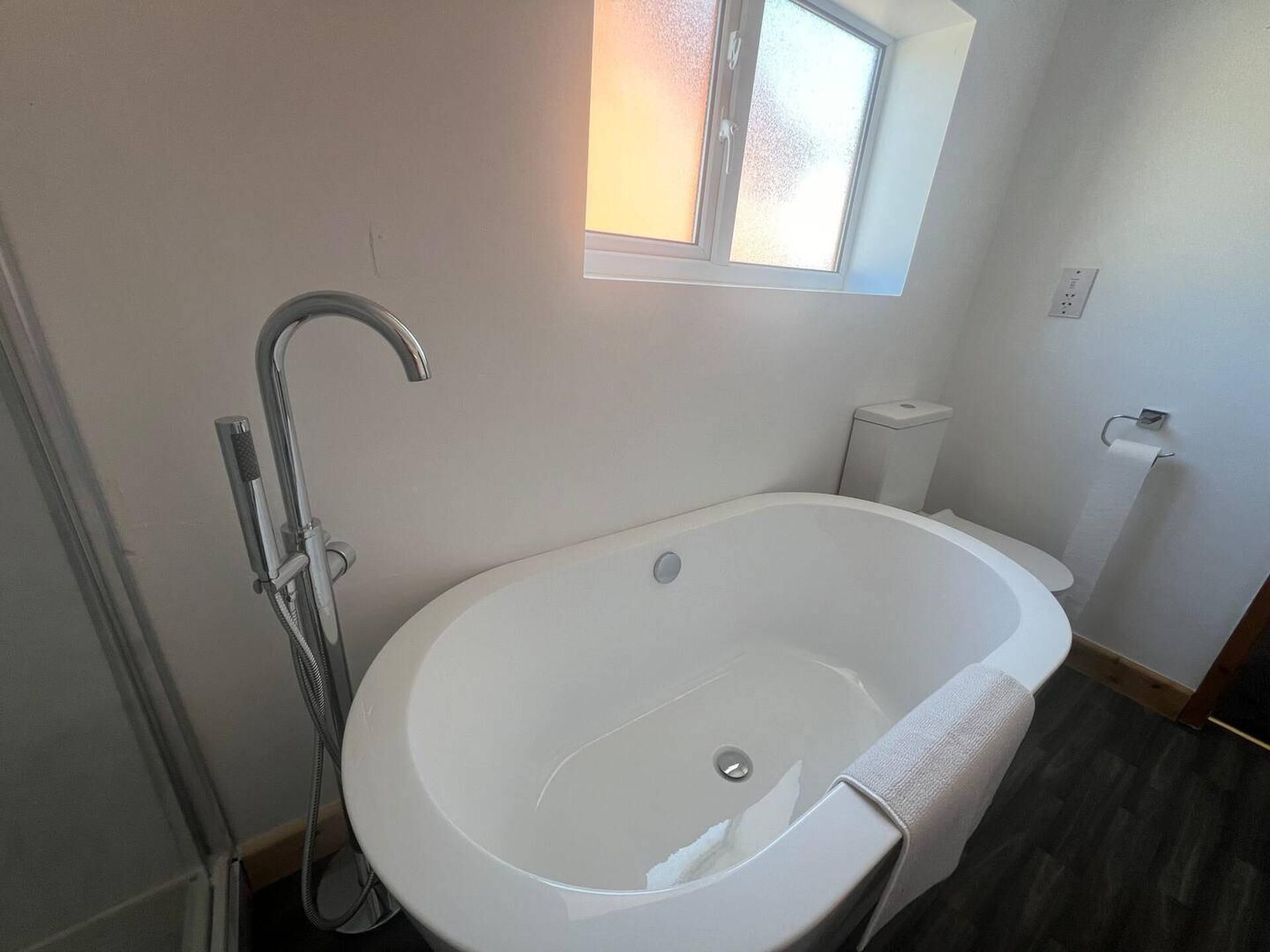 Un baño moderno con una bañera independiente, un cabezal de ducha y un ventanal que proporciona luz natural.