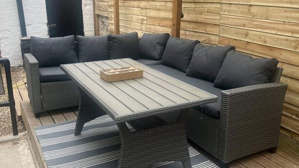 A sectional sofa with grey cushions and a wooden table, set on a wooden deck with a striped rug. - Blyton 2-bed Cottage, Parking, 30m to Lincoln (Gainsborough)