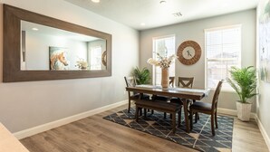 Un coin repas comprenant une table en bois, des chaises, un grand miroir et une horloge murale.
