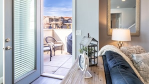 Une pièce dotée d’une porte-fenêtre coulissante qui donne sur un patio aménagé avec une chaise et un petit objet décoratif. Un canapé et une lampe se trouvent sur le côté droit.