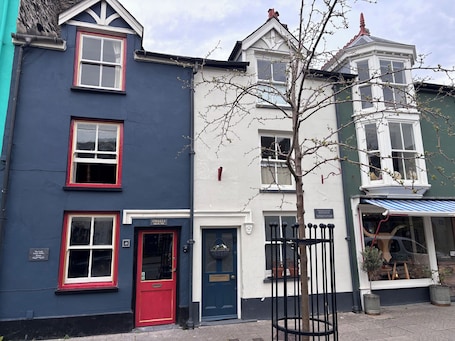 A row of buildings with distinct architectural styles, including a red door and a sign indicating 'Gwalior House.'. The Little Laura Ashley House