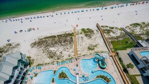 An aerial view of a beach resort with a large swimming pool, beach umbrellas, and a boardwalk.